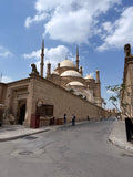 A grand mosque in Cairo, Egypt, with ornate arches and warm lighting, viewed from a street with pedestrians.