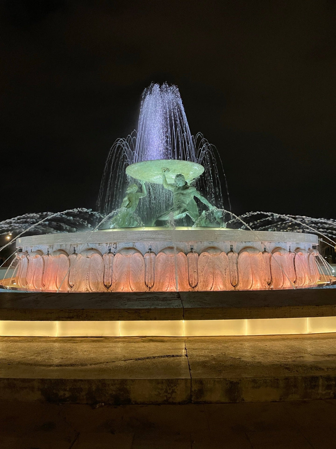 A grand fountain with sculpted figures is illuminated at night in Valletta, Malta.